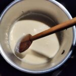 Creamy queso sauce in a pot with a long brown spoon